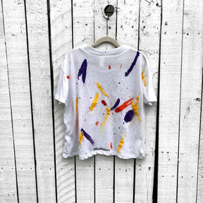 The perfect cropped white T shirt. Assorted color splatter and stripes painted on back, with small heart painted on front, upper left side in red. Signed @wrenandglory.