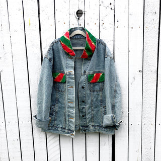 Lighter blue denim wash. UGLY CHRISTMAS JACKET painted in white, with black outline, on back. Ornaments, candy canes, mistletoe and other holiday related items decorating the letters. Collar and front pockets painted red and green, with gold boarders. Signed @wrenandglory.