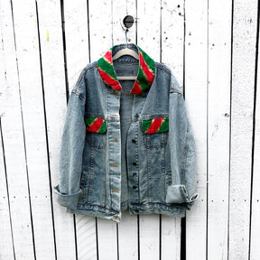 Lighter blue denim wash. UGLY CHRISTMAS JACKET painted in white, with black outline, on back. Ornaments, candy canes, mistletoe and other holiday related items decorating the letters. Collar and front pockets painted red and green, with gold boarders. Signed @wrenandglory.