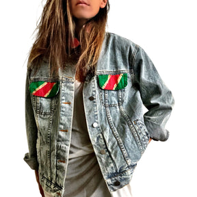 Lighter blue denim wash. UGLY CHRISTMAS JACKET painted in white, with black outline, on back. Ornaments, candy canes, mistletoe and other holiday related items decorating the letters. Collar and front pockets painted red and green, with gold boarders. Signed @wrenandglory.