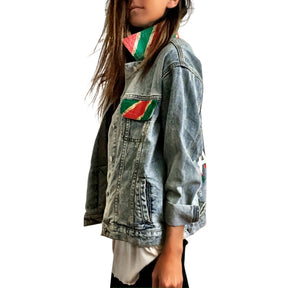 Lighter blue denim wash. UGLY CHRISTMAS JACKET painted in white, with black outline, on back. Ornaments, candy canes, mistletoe and other holiday related items decorating the letters. Collar and front pockets painted red and green, with gold boarders. Signed @wrenandglory.