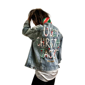 Lighter blue denim wash. UGLY CHRISTMAS JACKET painted in white, with black outline, on back. Ornaments, candy canes, mistletoe and other holiday related items decorating the letters. Collar and front pockets painted red and green, with gold boarders. Signed @wrenandglory.