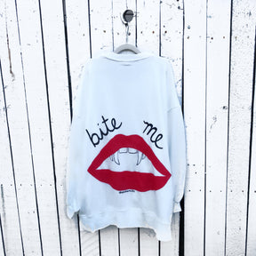 Oversized white sweatshirt. Lips and vampire teeth painted in on back, with with BITE ME painted above. Signed @wrenandglory.