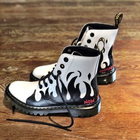 Black flames painted along the entire bottom of boots, with the words 'now you're walkin' painted in small font on one, and 'hummin your song' painted in small font on the other (in red on both). Painted on white Dr Marten boots.