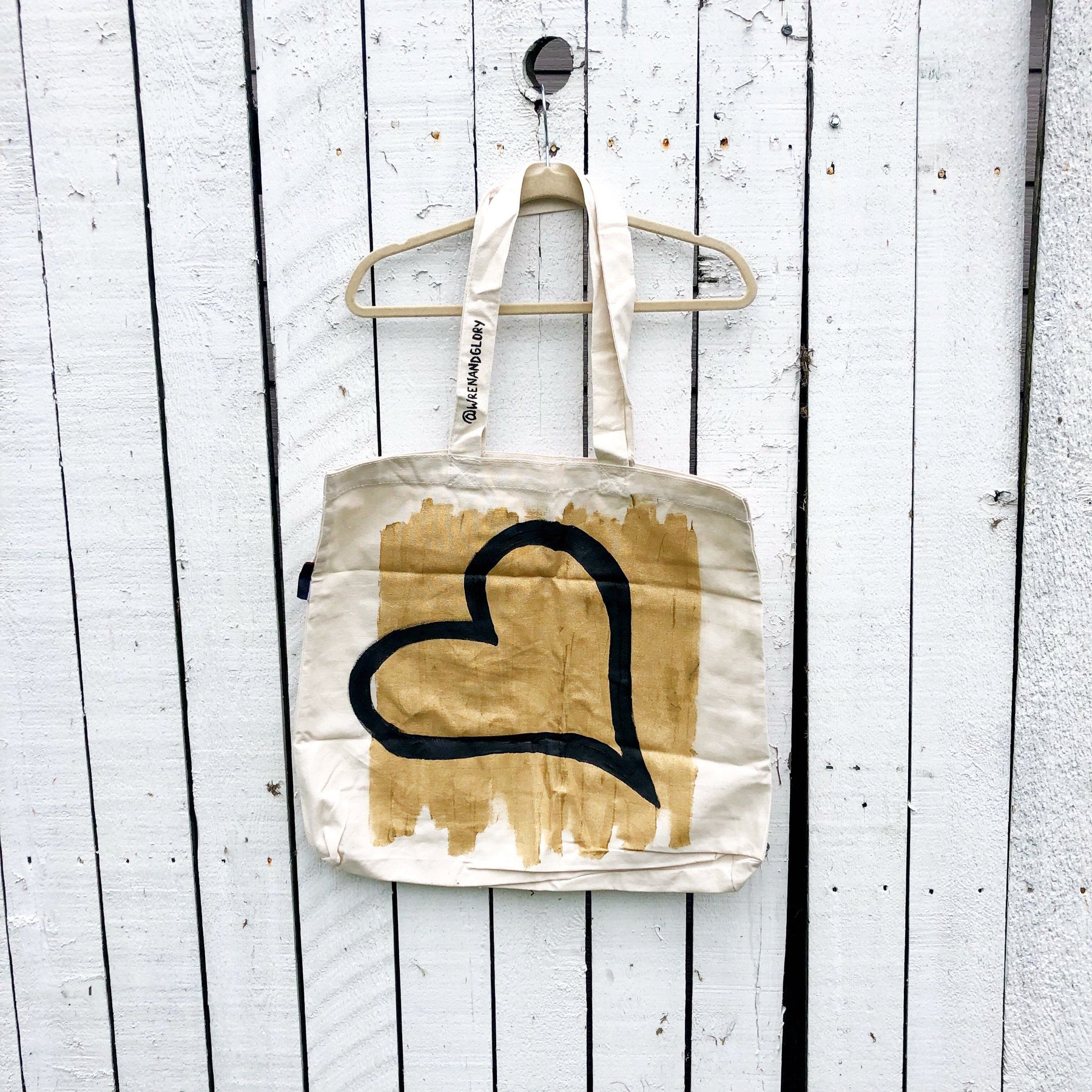 Off white canvas tote bag. Gold base, with large, black heart painted on diagonal. Signed @wrenandglory.